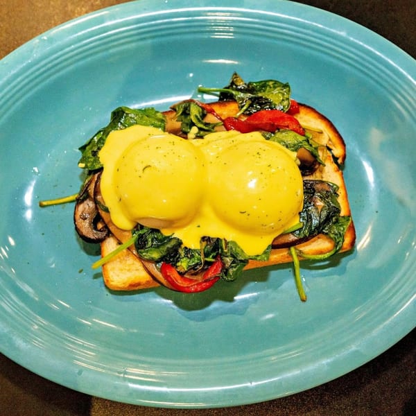 Eggs Benedict on toast with spinach, mushrooms, and red peppers on a blue plate.