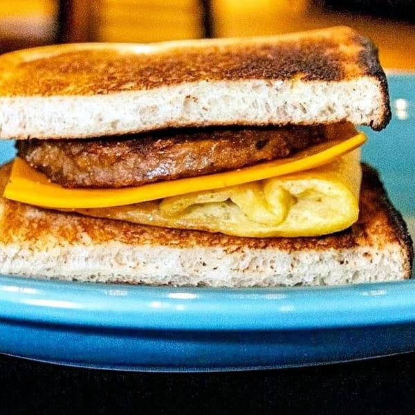 Breakfast sandwich with toasted bread, sausage patty, melted cheese, and folded egg on a blue plate.