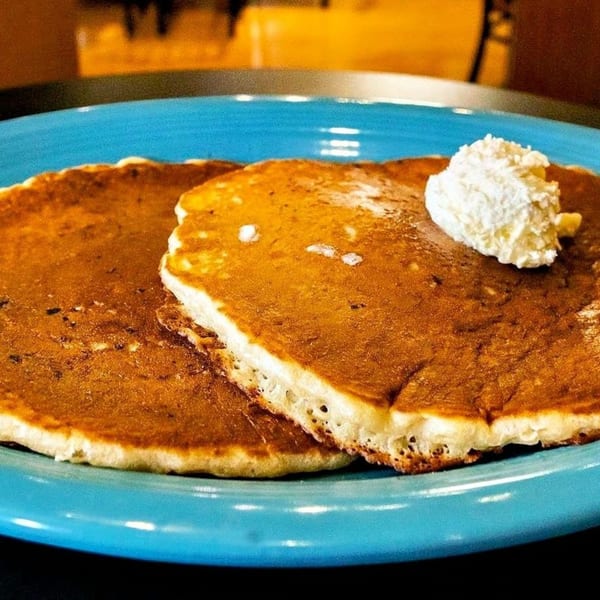 Two golden-brown pancakes with a dollop of whipped cream on a blue plate.